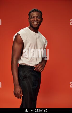 homme afro-américain ravi dans les vêtements de rue à la mode souriant à la caméra sur rouge, positivité Banque D'Images