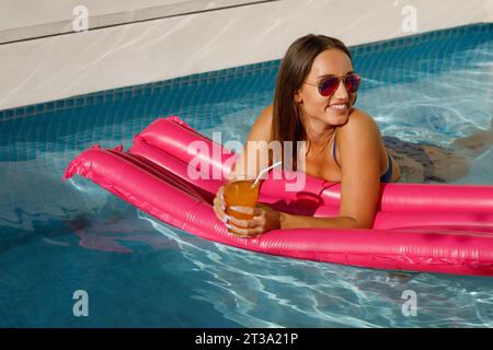 Sunkissed Beauty : Dame élégante appréciant le temps de la piscine sur Pink Float Banque D'Images