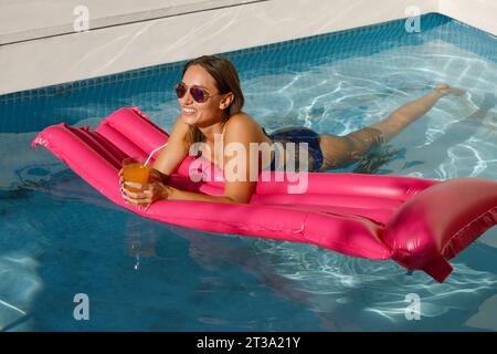 Relaxation et Radiance : Femme à la mode dans la piscine avec flotteur rose Banque D'Images