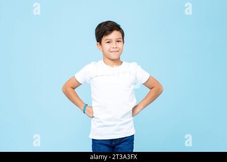 Mignon garçon de race mixte souriant avec des bras akimbo en studio isolé fond de couleur bleu clair Banque D'Images