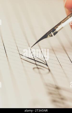 la main féminine écrit avec le stylo inky sur une feuille de papier blanche avec des rayures. papeterie sur le bureau vue rapprochée du dessus. leçons d'orthographe et calligraphie effort Banque D'Images