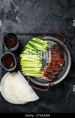 Canard de Pékin servi avec du concombre, des oignons verts et des crêpes chinoises de lactosérum rôties à la sauce Hoysin. Arrière-plan noir. Vue de dessus. Banque D'Images