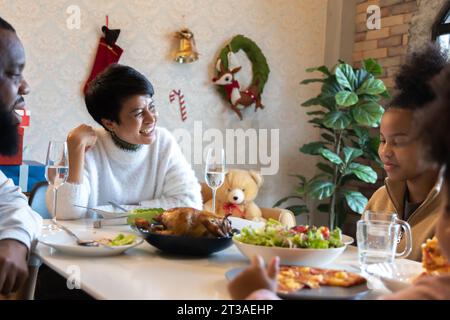 Portrait d'une jeune femme avec un mari afro-américain appréciant le déjeuner de noël de la turquie dans une maison décorée avec des bas, la canne à sucre, la couronne, des cadeaux et des cloches Banque D'Images