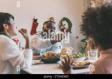 Portrait de jeune homme avec mari afro-américain appréciant le déjeuner de noël de la turquie à la maison décorée avec des bas, canne à sucre, couronne, cadeaux et cloches Banque D'Images