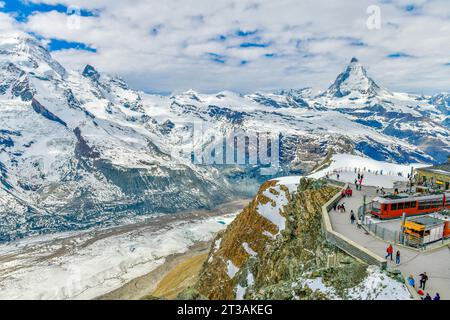 Train rouge sur le chemin de fer enneigé à la gare du sommet avec les touristes et le sommet du Cervin et le glacier Gorner en Suisse Banque D'Images