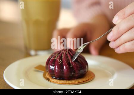 Femme mangeant délicieux gâteau de mousse de myrtille fraîche. Couper la texture du dessert en gros plan. Personne prenant une tranche de cheesecake pourpre dans un restaurant, c Banque D'Images