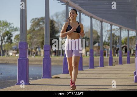 Fille latine court par une pergola dans un parc public. Banque D'Images