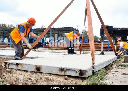 Les constructeurs dans les casques de sécurité travaillent sur le chantier de construction. L'équipe de travailleurs pose la dalle de béton sur le sol le jour de l'été. De vrais travailleurs. Contexte. Banque D'Images