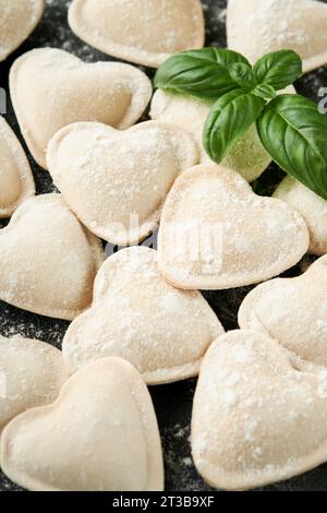 Pâtes ravioli italiennes en forme de coeur. Ravioli crus savoureux avec de la farine et du basilic sur fond sombre. Fond des ingrédients de cuisson des aliments. Valentines ou Mo Banque D'Images