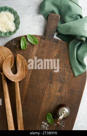 Planche à découper avec cuillères de cuisine et serviette rouge et persil, tomate pour cuisiner sur fond sombre en bois ancien. Cuisine végétarienne, santé ou cuisine con Banque D'Images