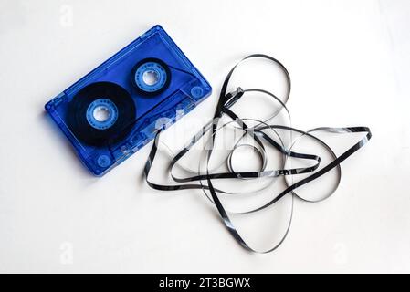 Gros plan d'une vieille cassette audio bleue avec la bande magnétique dépassant et emmêlée sur fond blanc. Banque D'Images