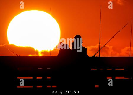 Île de Palms, États-Unis. 24 octobre 2023. Les pêcheurs silhouettés par le lever du soleil attendent que le poisson morde sur la jetée de l'île de Palms, le 24 octobre 2023 à l'île de Palms, en Caroline du Sud. Crédit : Richard Ellis/Richard Ellis/Alamy Live News Banque D'Images