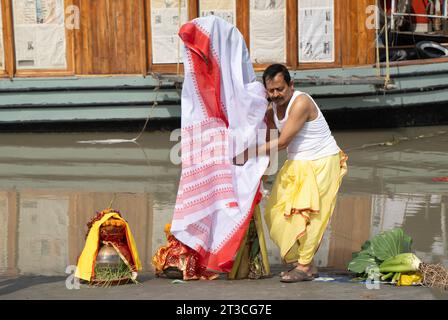 Un dévot debout avec un bananier décoré traditionnellement enveloppé dans un sari, symbolisant l'épouse du Dieu hindou Ganesha, alors qu'il arrive pour s'immerger dans la rivière Brahmapoutre à la fin du festival Durga Puja ou Dashami, le 24 octobre 2023 à Guwahati, Assam, Inde. Durga Puja est l'un des festivals les plus importants en Inde. Crédit : David Talukdar/Alamy Live News Banque D'Images