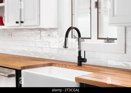 Un détail de robinet de cuisine avec des armoires blanches, un comptoir de bloc de boucher, et un dosseret de tuile de métro blanc. Banque D'Images