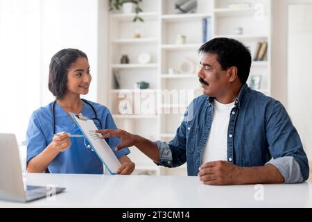 Femme médecin indienne montrant Clipboard avec enquête médicale à patient mâle mature Banque D'Images