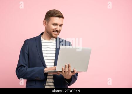 Souriant homme d'âge moyen détendu dans le look de bureau tenant l'ordinateur portable isolé sur fond rose Banque D'Images