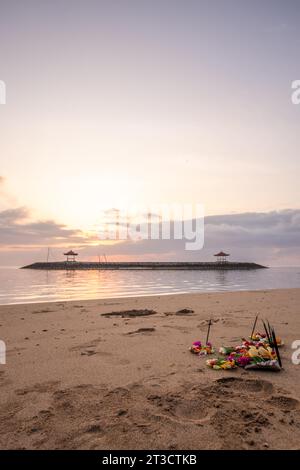 Lever de soleil sur une plage de sable avec de petits temples dans l'eau. Paysage photographié avec des offrandes de prières hindoues traditionnelles sur la plage de Sanur, Bali Banque D'Images