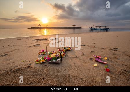 Lever de soleil sur une plage de sable avec de petits temples dans l'eau. Paysage photographié avec des offrandes de prières hindoues traditionnelles sur la plage de Sanur, Bali Banque D'Images