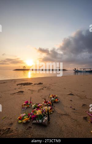 Lever de soleil sur une plage de sable avec de petits temples dans l'eau. Paysage photographié avec des offrandes de prières hindoues traditionnelles sur la plage de Sanur, Bali Banque D'Images