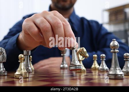 Homme avec la pièce de jeu jouant aux échecs à l'échiquier à l'intérieur, gros plan Banque D'Images