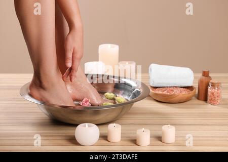 Femme trempant ses pieds dans un bol avec de l'eau et des fleurs sur la surface en bois, gros plan. Procédé de pédicure Banque D'Images