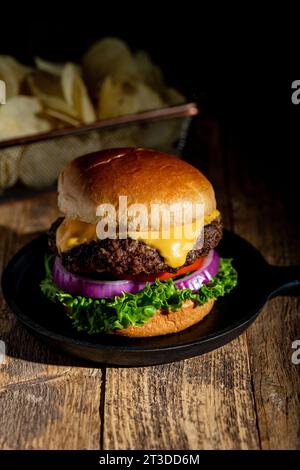 Cheeseburger chaud frais foncé et de mauvaise humeur avec brioche brioche et chips de pommes de terre en arrière-plan Banque D'Images