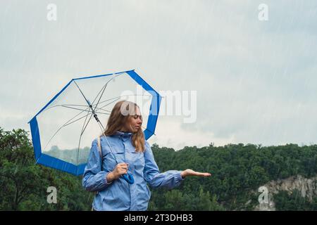 Fille blonde vérifiant le temps sous un parapluie transparent à l'extérieur dans le parc. Heure d'automne pluvieux mauvaises conditions de prévision saison. Touriste avec parapluie voyage dans de nouveaux endroits sous la pluie. Paysage Banque D'Images