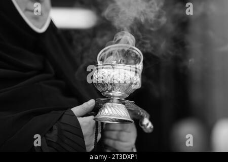 Faible profondeur de champ (mise au point sélective) détails avec la main d'une religieuse chrétienne orthodoxe tenant un brûleur d'encens censer métallique fumant Banque D'Images