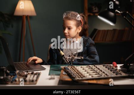 Mignon fille intelligente est passionnée de réparer une carte mère, faire de l'électronique, connecter des fils, souder des câbles tard dans la nuit Banque D'Images