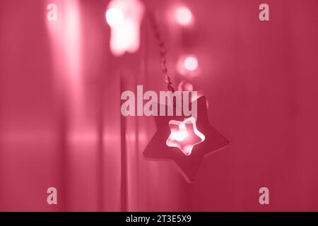Guirlande de lumières de Noël en forme d'étoile colorée Viva Magenta accrochée à un mur. Gros plan, mise au point sélective. Intérieur. Maison confortable. Nouvel an, ambiance de Noël. Banque D'Images