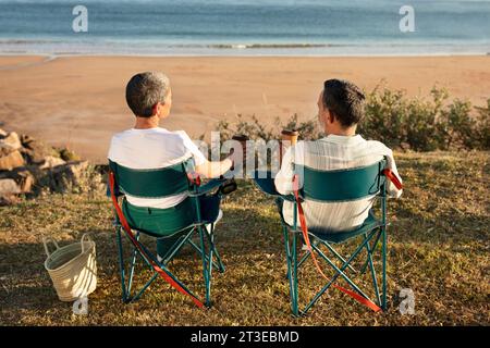 Couple plus âgé assis ensemble face à l'océan appréciant un café au bord de la mer Banque D'Images