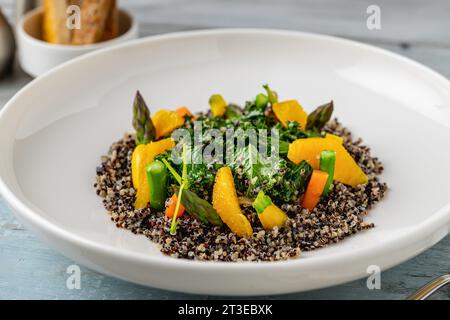 Salade de quinoa avec des feuilles d'orange et de chou frisé sur une assiette en porcelaine blanche sur une table en bois Banque D'Images