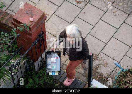 Une femme transporte son recyclage dans le bac de recyclage à l’extérieur de sa maison à Lambeth, le 20 octobre 2023, à Londres, en Angleterre. Banque D'Images