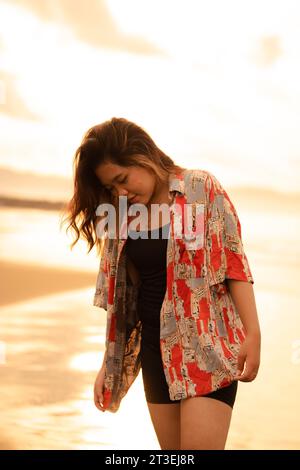 Une femme asiatique aux cheveux blonds et une chemise rouge marche le long de la plage pour profiter de la vue sur la mer dans l'après-midi Banque D'Images