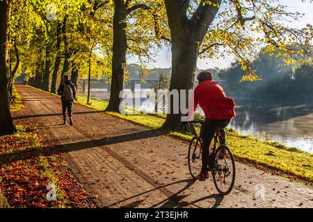 Preston, Lancashire. UK Météo. 25 octobre 2023. Fin lumineux mais brumeux commencent à la journée comme le soleil d'automne se lève sur la rivière Ribble. Les résidents locaux font de l'exercice léger le long de la promenade bordée d'arbres au bord de la rivière à Avenham Park. Crédit MediaWorlImages/AlamyLiveNews Banque D'Images