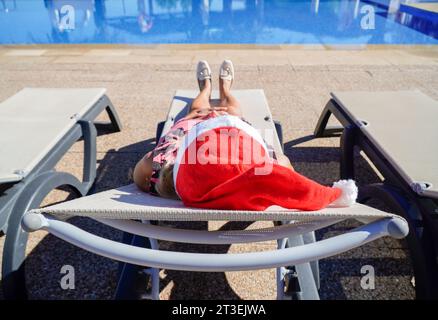 femme mature avec chapeau de père noël couché dans une chaise longue de plage à noël. Noël en été Banque D'Images