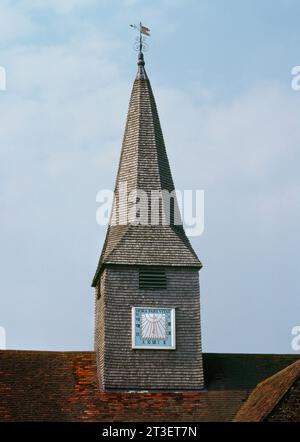 Montez le cadran solaire sur la face S de la tourelle de la cloche avec une flèche de broche sur le toit en tuiles de l'église St Michael and All Angels, Thursley, Surrey, Angleterre. Banque D'Images