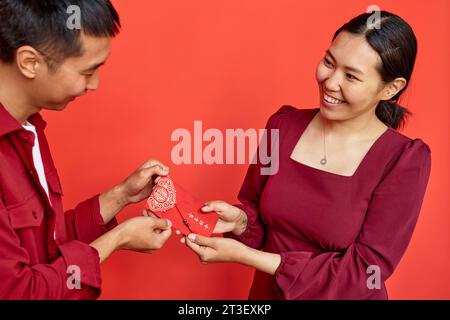 Portrait de jeune couple asiatique donnant enveloppe rouge hongbao avec inscription bonne chance comme présent pour le nouvel an chinois, l'espace copie ont débordant d'abondance chaque année Banque D'Images