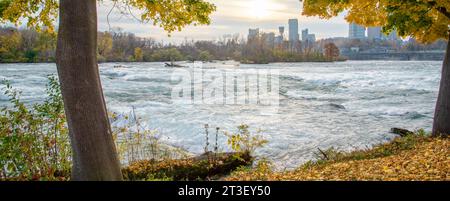 Panorama feuillage d'automne jaune vif feuilles d'automne de Goat Island, en amont des chutes Niagara avec le centre-ville de Niagara Falls City, Canada en arrière-plan à s Banque D'Images