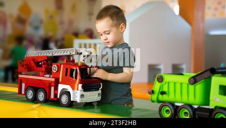 Mignon garçon en bas âge jouant avec des voitures dans la salle de jeux pour enfants. Mode de vie actif, enfance. Mise au point sélective Banque D'Images