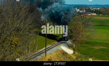 Une vue aérienne d'un train de passagers à vapeur profilé voyageant à travers des terres agricoles fertiles soufflant de la fumée noire un jour d'automne Banque D'Images