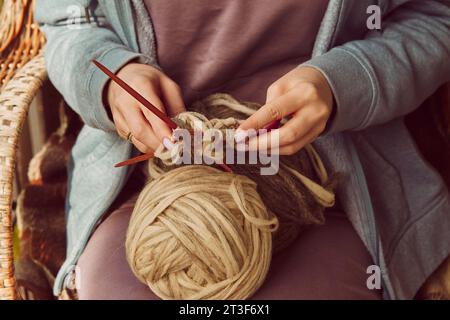 Les mains de femme tricotent avec des aiguilles à tricoter et des fils de laine se rapprochent. Fond de bricolage. Occupation chaleureuse d'automne confortable. Banque D'Images