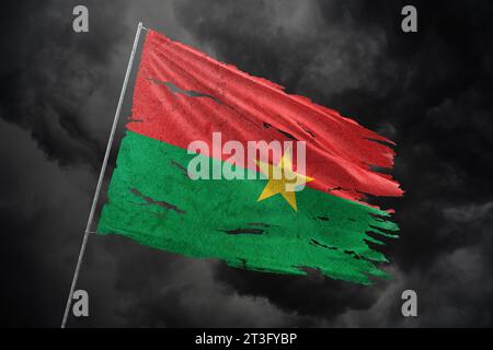 Burkina Faso drapeau déchiré sur fond de ciel sombre. Banque D'Images