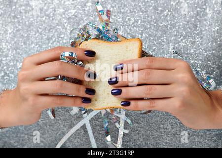 Gros plan d'une femme recadrée tenant un sandwich avec des guirlandes sur fond gris, concept Happy New Year Banque D'Images