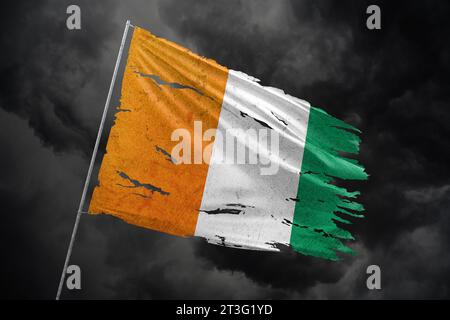 Drapeau déchiré de la Côte d'Ivoire sur fond de ciel sombre. Banque D'Images