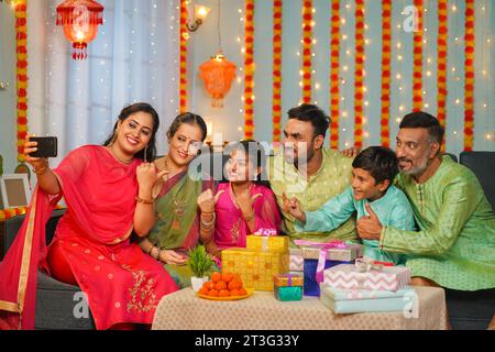 Groupe de membres de la famille commune prenant selfie sur téléphone portable pendant le festival diwali rassemblement à la maison - concept de réunion, génération et spécial Banque D'Images