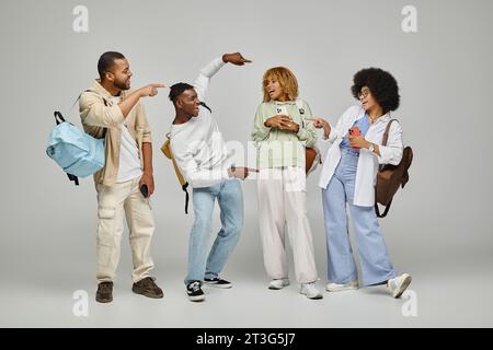 heureux élèves riant en tenue décontractée avec des sacs à dos pointant les doigts activement, étudiant le concept Banque D'Images