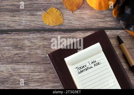 Aujourd'hui, je suis reconnaissant pour, le texte manuscrit dans un petit carnet, la bible sainte, la citrouille, et les feuilles d'automne sur la table en bois. Vue de dessus. Gratitude chrétienne. Banque D'Images