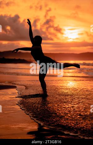 Silhouette d'une femme asiatique dansant un ballet avec une grande flexibilité et une vue sur les vagues derrière elle au coucher du soleil Banque D'Images