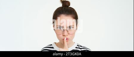 Image d'une femme sérieuse dans des lunettes, professeur qui chie, fait chir, faire taire le geste, appuyer le doigt sur les lèvres et froncer les sourcils de désapprobation, se tenir debout Banque D'Images